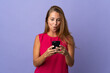 © luismolinero - Middle age brazilian woman isolated on purple background looking at the camera while using the mobile with surprised expression