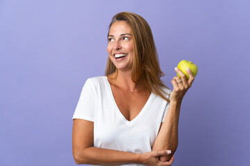 Middle age brazilian woman isolated on purple background with an apple and happy