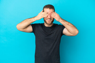 Sticker - Young handsome caucasian man isolated on blue background covering eyes by hands and smiling