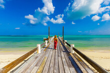 Woman Walking Up The Pier That Stretches Out Into The Ocean From Horse Stable Beach, North Caicos, Turks And Caicos Islands, Atlantic, Central America