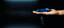 Hand Holding Miniature Automobile Model And Key On Dark Background. Car Buying And Rental. Banner