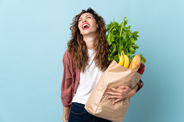 Wall Mural - Young woman holding a grocery shopping bag isolated on blue background laughing