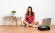 © luismolinero - Young woman with a laptop sitting on the floor at indoors thinking and sending a message