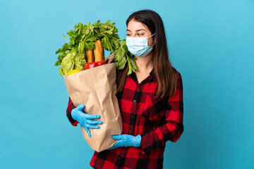 Young caucasian with vegetables and mask isolated on blue background with happy expression