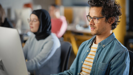Fototapete - Portrait of a Handsome Smart Male Student in Glasses, Studying in Modern University with Diverse Multiethnic Classmates. Works on Computer in College. Applying His Knowledge and Skills.