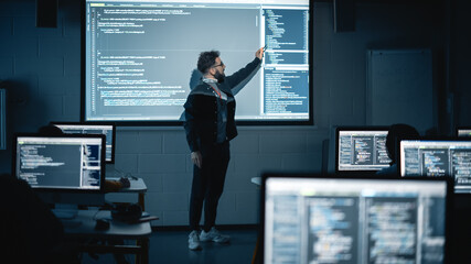 Fototapete - Teacher Giving Computer Science Lecture to Diverse Multiethnic Group of Female and Male Students in Dark College Room. Projecting Slideshow with Programming Code. Explaining Information Technology.