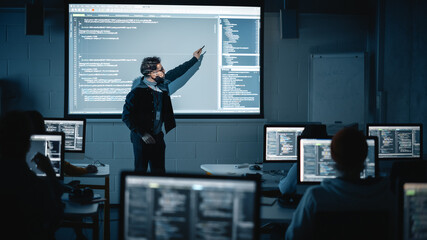 Fototapete - Teacher Giving Computer Science Lecture to Diverse Multiethnic Group of Female and Male Students in Dark College Room. Projecting Slideshow with Programming Code. Explaining Information Technology.