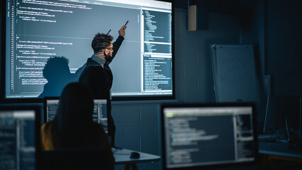 Fototapete - Teacher Giving Computer Science Lecture to Diverse Multiethnic Group of Female and Male Students in Dark College Room. Projecting Slideshow with Programming Code. Explaining Information Technology.