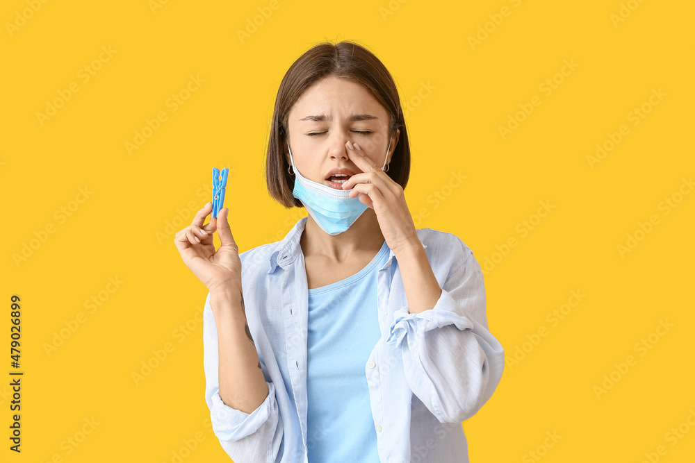 Ill young woman with clothespin on color background. Stuffy nose concept