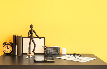 Workplace with tablet computer, stationery supplies, eyeglasses and mannequin doll near color wall