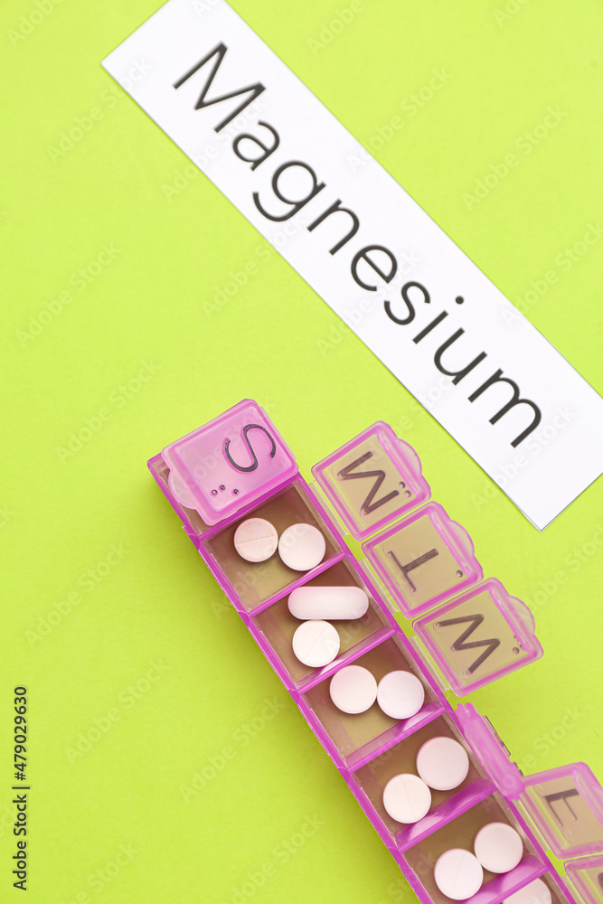 Plastic container with pills and word MAGNESIUM on green background