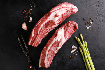 Wall Mural - Raw meat. Steak beef  with spices, rosemary, asparagus, garlic on a black table. Background image, copy space, flatlay, top view