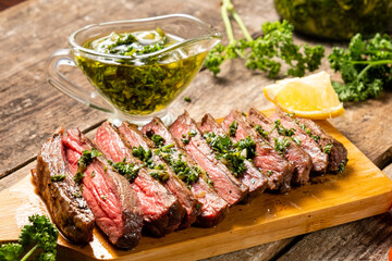 Appetizing beef steak cooked and sliced on a wooden table with chimichurri sauce.