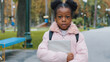 © Yuliia - Close-up afro child standing with book in hand in park schoolgirl seriously looking at camera portrait african american kid with hairstyle and black backpack after school outdoors pupil get education