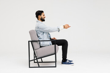 Side view of Asian man sitting in the armchair while watching television in the studio