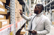 © Art_Photo - Portrait of smiling african american business man order details on tablet checking goods and supplies on shelves with goods background in warehouse.logistic and business export