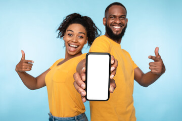 Wall Mural - cheerful black couple pointing at smartphone with mockup on screen, recommending mobile app, adverti