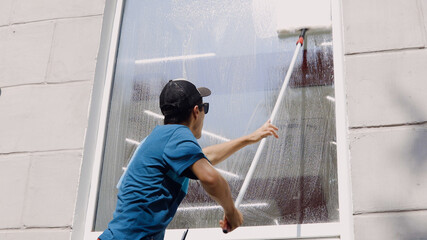 Wall Mural - An employee of a professional cleaning service in overalls washes the glass of the windows of the facade of the building. Showcase cleaning for shops and businesses