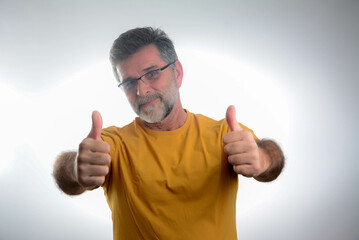 Wall Mural - Mature handsome man wearing casual t-shirt standing over isolated grey background success sign doing positive gesture with hand, thumbs up smiling and happy. Cheerful expression and winner.