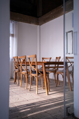 Stylish modern loft dining area with natural light scene and bare concrete wall with natural wood table and chairs setting / interior design