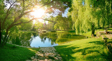Beautiful Colorful Summer Spring Natural Landscape With A Lake In Park Surrounded By Green Foliage Of Trees In Sunlight And Stone Path In Foreground.