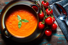 Home Made Tomato Soup Served On A Rustic Wooden Table And Garnished With Basil And Vine Ripened Tomatoes.