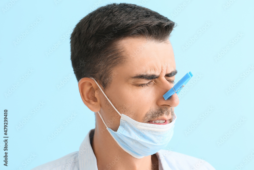 Ill young man with clothespin on his nose against color background