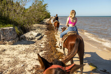 View From Behind Of Family Riding Horses On Tropical Island Beach Of Mexico