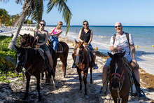 Family Of Four Riding Horses On Tropical Island Beach Of Mexico For Fun Vacation Together.