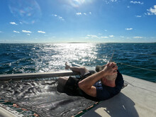 A Man Sits In A Hammock On The Bow Of A Catamaran Boat Taking In The View Of The Caribbean Sea Off The Coast Of Cozumel, Mexico During A Vacation Sail In The Sun
