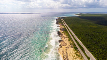 Aerial Drone View Of Coastal Highway Adjacent To Dense Jungle And Caribbean Sea On The Tropical Island Of Cozumel, Mexico. The Ocean Waves Are Crashing Against The Sandy Beach.