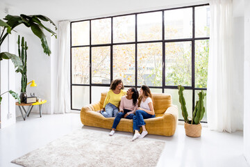 Indoor shot of three happy young women sitting on sofa - Young multiracial female friends hanging out and relaxing at home - Social gathering, friendship, youth and millennial people concept