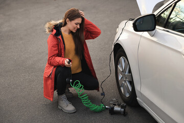 Wall Mural - Young woman trying to inflate car tire with air compressor on street