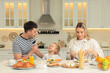 © New Africa - Happy family having breakfast together at table in kitchen