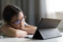 Asian Child Bored To Sleepy Lie Down On Desk In Study Online Class Or Kid Girl Student Back To School Wearing Eyeglasses To Unhappy Learning On Computer Tablet By Video Call Or Person Learn From Home