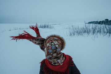 A girl wearing a Russian folk shawl stands on the shore of the White Sea in winter