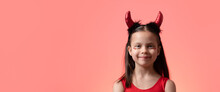 Little Smiling Girl With Pigtails And Red Shiny Tiny Hearts Under Her Eyes In Costume Of Little Devil Against Peachy Background