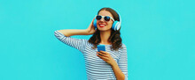 Portrait Of Smiling Young Woman In Headphones Listening To Music With Smartphone On Blue Background