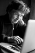 © De Visu - An senior woman working on the computer in her home. Black and white photo.