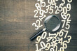 Magnifying glass in scattered numbers on wood background, calculation, mathematics concept