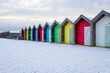 A row of vibrant, brightly coloured beach huts taken in winter with snow on the ground. Blyth, Northumberland - UK