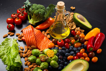 Healthy diet and nutrition food rich in vitamins and omega-3 concept, assorted fresh vegetables, green salad, fruit, fish salmon, nuts, blueberries, bottle of olive oil on black chalk board background