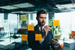 © Liubomir - Successful businessman rewrites a task on a glass board with colored stickers, from phone and tablet