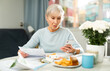 © JackF - Senior woman sitting at table and trying to pay her bills with smartphone at home.
