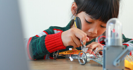 The little girl asian building robotic car in science lesson in the house . Which increases the development and enhances learning skills gifted brilliant children working with technology.