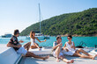 Group of Caucasian people friends enjoy luxury party drinking champagne together while catamaran boat sailing in the ocean. Man and woman relax outdoor lifestyle sail yacht on tropical travel vacation