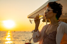 Caucasian Woman Enjoy Outdoor Luxury Lifestyle With Drinking Champagne While Catamaran Boat Sailing At Summer Sunset. Beautiful Female Relaxing Outdoor Leisure Activity With Tropical Travel Vacation