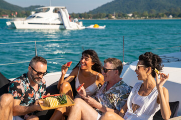 group of man and woman friends enjoy outdoor party eating fresh fruit together while catamaran boat 