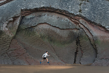 Wall Mural - Teenager running and jumping on the sand in front of impressive cliff wall. Training outdoors in beautiful landscapes concept.