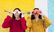 © Westend61 - Playful sisters covering eyes with vegetables in front of multi colored wall
